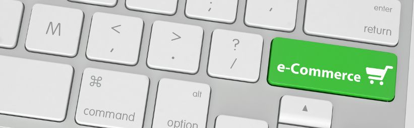 Conceptual Green E-Commerce Button with Small Cart Design on a White Computer Keyboard Placed on White Table. Captured in Close up High Angle View.