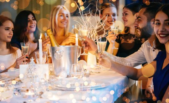 Friends celebrating Christmas or New Year eve. Party table with champagne.