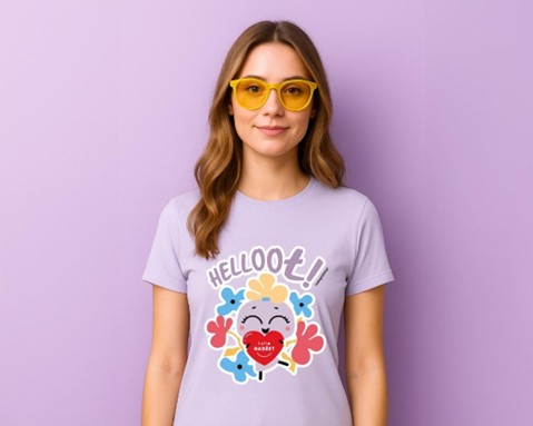 Uśmiechnięta kobieta w żółtych okularach i fioletowej koszulce z kolorową grafiką maskotki Hellogadżet oraz napisem „HELLOO Ł!” – na tle ściany w pastelowym, fioletowym odcieniu.